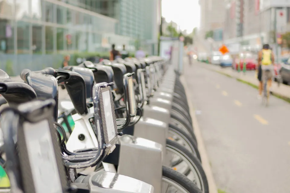 Close-up of silver Bixi bike share bikes parked at a station in Montreal, Quebec, Canada with blurred person on bike riding away in background.